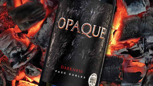 Closeup of bottle of Opaque Darkness wine atop red hot coals